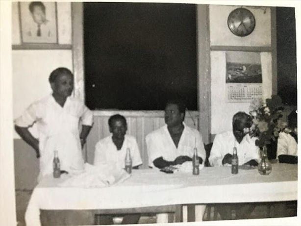 Black and white archive photograph of men in white seated along a long table at an early gathering of the association, one standing to address the room.