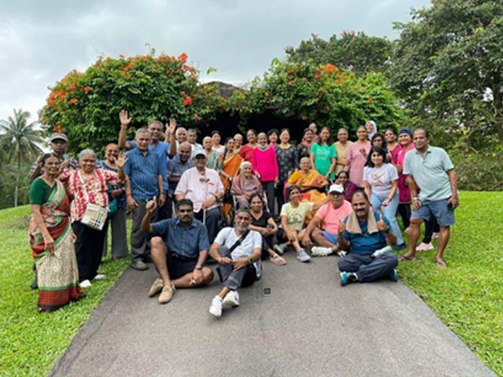 Around forty members of Singai Namakkal Sangam, from children to seniors, gathered on a lawn at the Singapore Botanic Gardens, several waving at the camera.