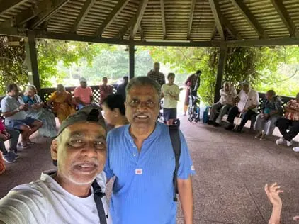 Two members take a selfie with seniors gathered in the pavilion behind them
